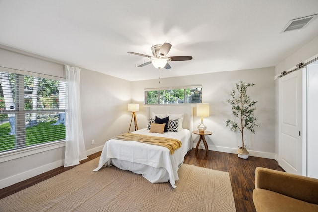 bedroom featuring a barn door, baseboards, visible vents, and wood finished floors