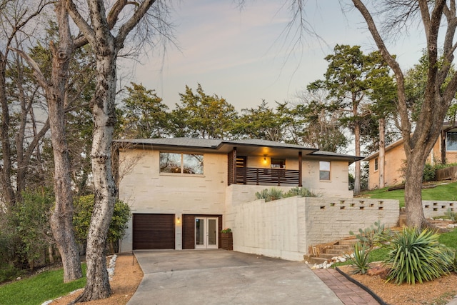 view of front of house featuring french doors, an attached garage, driveway, and a balcony