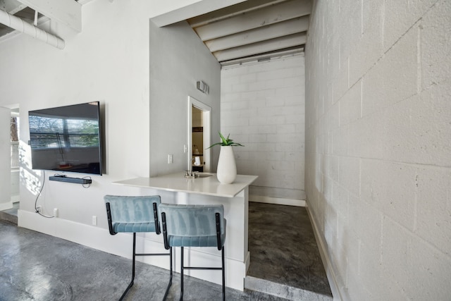 interior space with a high ceiling, concrete flooring, a breakfast bar, and concrete block wall