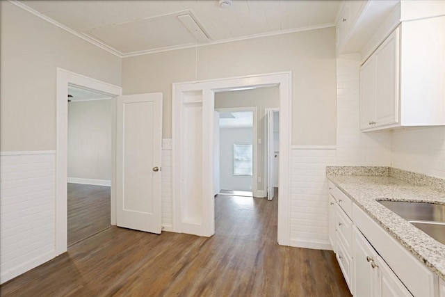 kitchen with dark wood-type flooring, light stone counters, white cabinetry, crown molding, and wainscoting