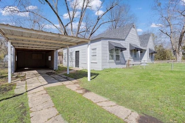 view of side of property featuring driveway, fence, a yard, a shingled roof, and a carport