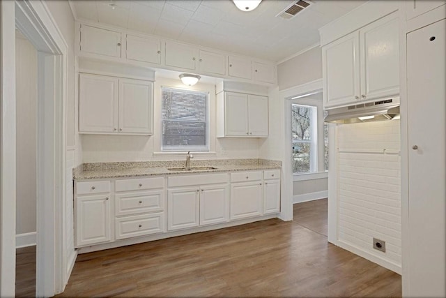 kitchen with under cabinet range hood, white cabinetry, light wood-style floors, and a sink