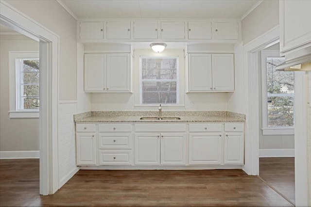 kitchen with light stone countertops, dark wood finished floors, ornamental molding, white cabinetry, and a sink