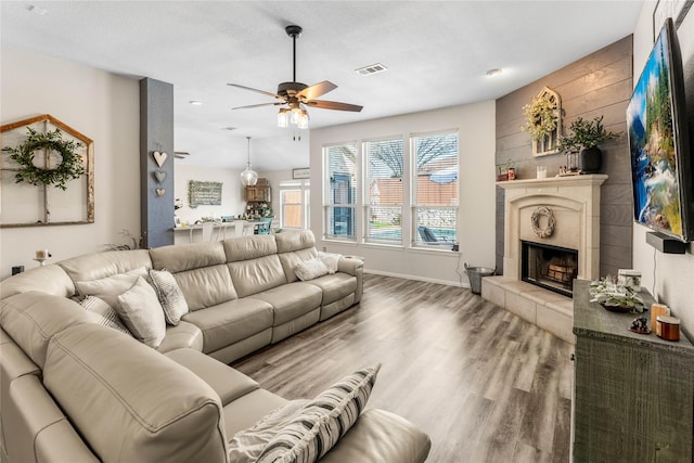 living room with visible vents, a ceiling fan, a tiled fireplace, wood finished floors, and baseboards