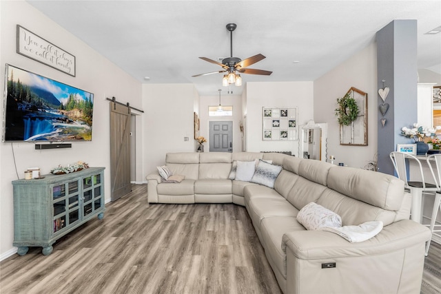 living room with ceiling fan, a barn door, and wood finished floors