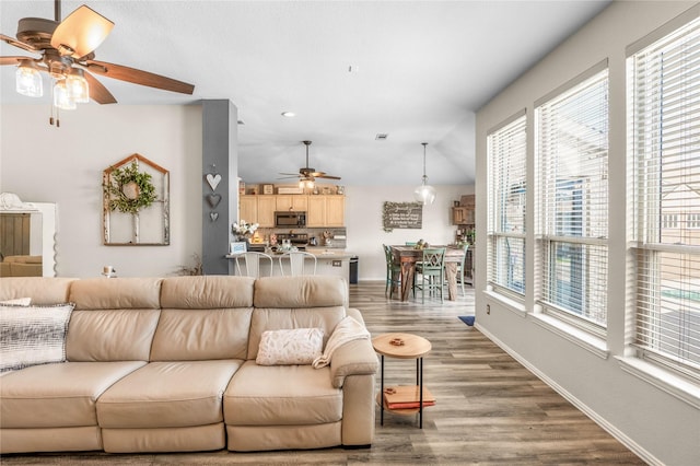 living area with visible vents, baseboards, ceiling fan, vaulted ceiling, and wood finished floors