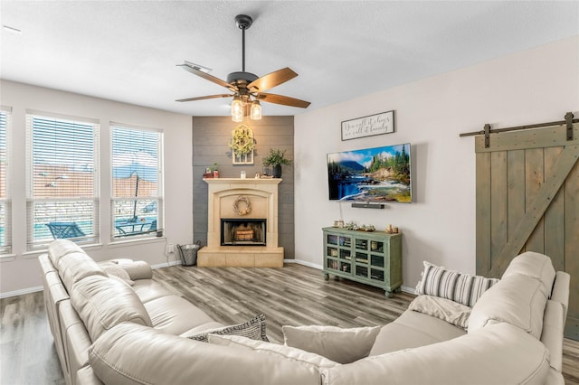 living area with a ceiling fan, wood finished floors, baseboards, a fireplace, and a barn door