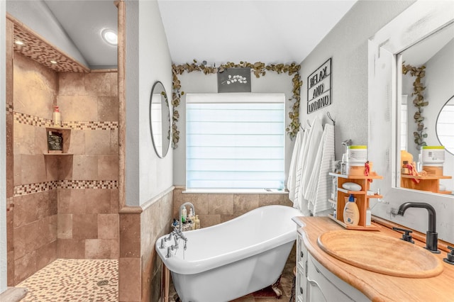 full bathroom featuring vanity, a freestanding tub, vaulted ceiling, walk in shower, and tile walls