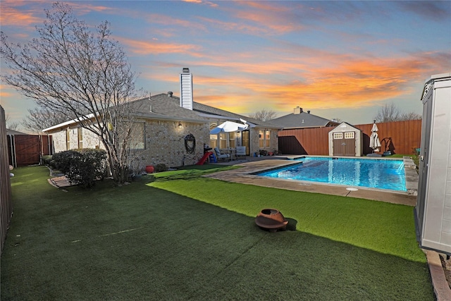 view of pool with an outbuilding, a fenced in pool, a yard, a fenced backyard, and a storage unit