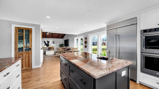 kitchen featuring a sink, a center island, dark stone counters, appliances with stainless steel finishes, and white cabinets