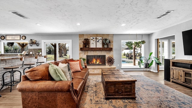 living room with a stone fireplace, wood finished floors, and visible vents