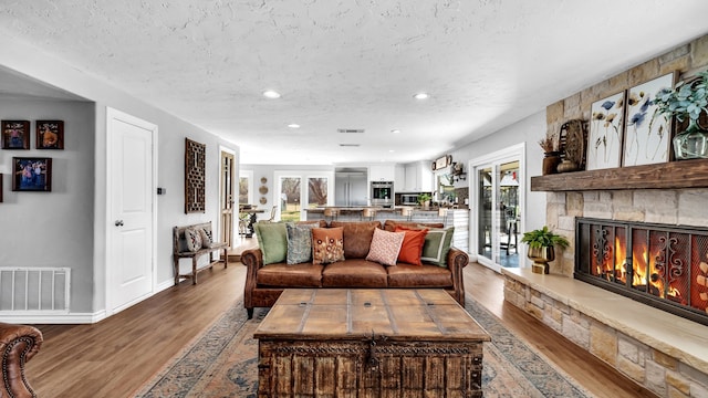 living area featuring visible vents, a textured ceiling, wood finished floors, recessed lighting, and a stone fireplace