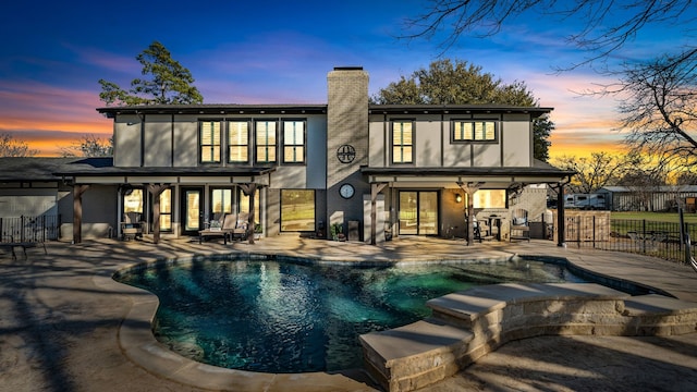 rear view of property with fence, a pool with connected hot tub, a chimney, a patio area, and brick siding