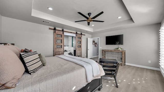 bedroom featuring wood finished floors, baseboards, visible vents, a barn door, and a raised ceiling