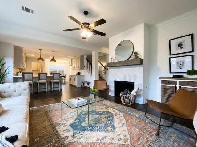 living room featuring visible vents, crown molding, ceiling fan, dark wood finished floors, and a premium fireplace