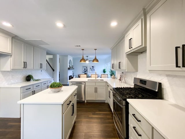 kitchen with a sink, dark wood finished floors, appliances with stainless steel finishes, a peninsula, and light countertops