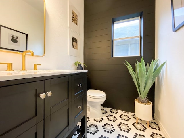 half bath featuring wooden walls, toilet, vanity, and baseboards