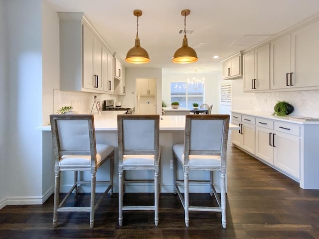 kitchen featuring backsplash, dark wood-type flooring, a breakfast bar, light countertops, and a peninsula