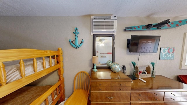 bedroom with a textured ceiling, a wall mounted air conditioner, and a textured wall