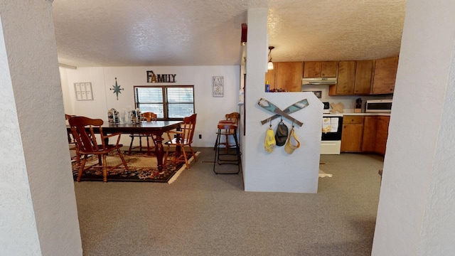 kitchen with under cabinet range hood, light carpet, range with electric stovetop, brown cabinetry, and a textured ceiling