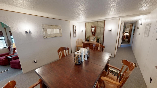 carpeted dining area with a textured ceiling and a textured wall