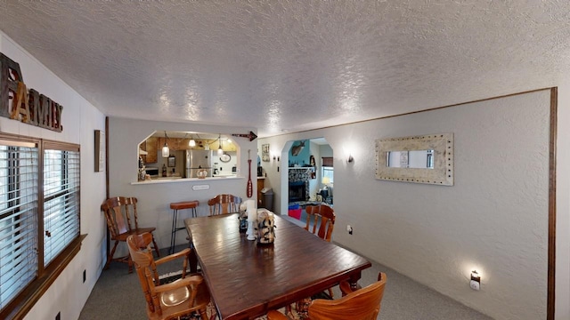 carpeted dining area featuring arched walkways, a textured ceiling, and a textured wall