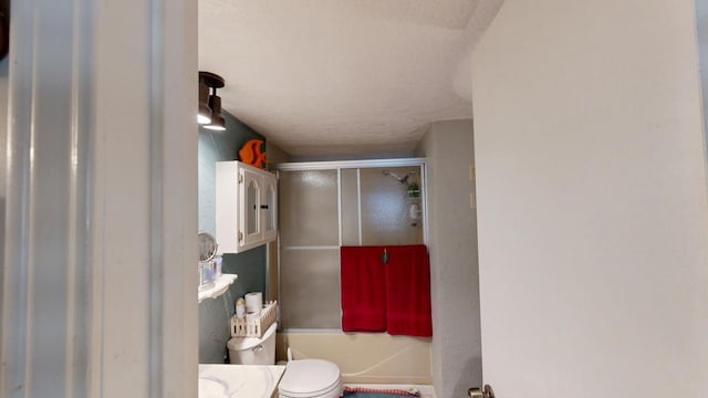 bathroom with toilet, combined bath / shower with glass door, and a textured ceiling