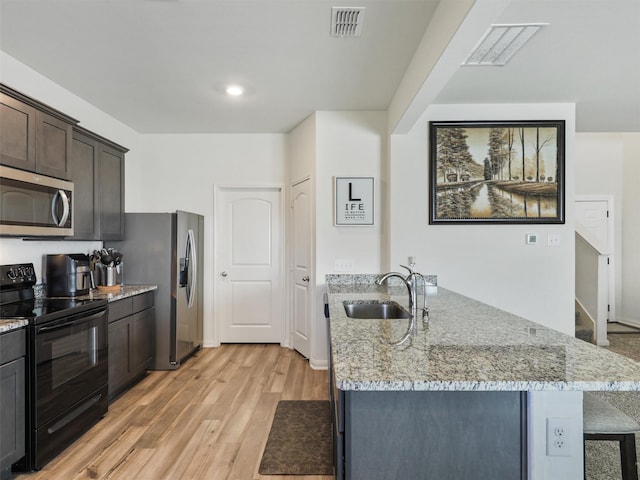 kitchen featuring visible vents, light wood-style flooring, a peninsula, stainless steel appliances, and a sink