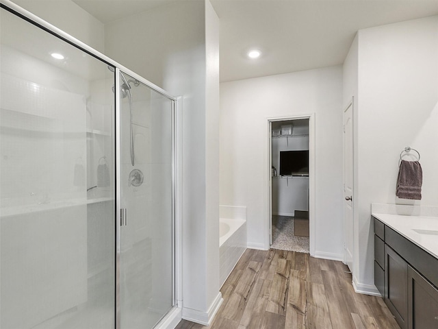 full bath featuring a shower stall, vanity, a garden tub, and wood finished floors