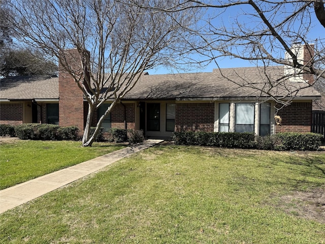 ranch-style house with a front lawn, brick siding, roof with shingles, and a chimney