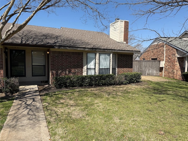 view of front of house with brick siding, fence, a front yard, roof with shingles, and a chimney