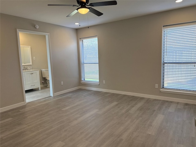 unfurnished bedroom featuring light wood-style flooring, a sink, recessed lighting, connected bathroom, and baseboards