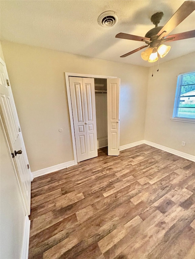 unfurnished bedroom featuring wood finished floors, visible vents, baseboards, a closet, and a textured ceiling