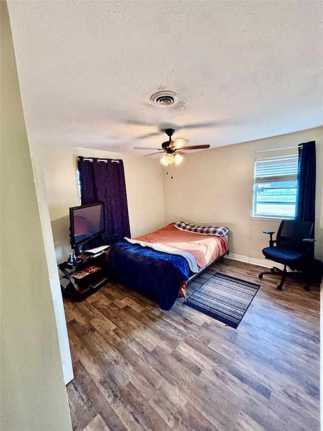 bedroom with wood finished floors, baseboards, visible vents, ceiling fan, and a textured ceiling