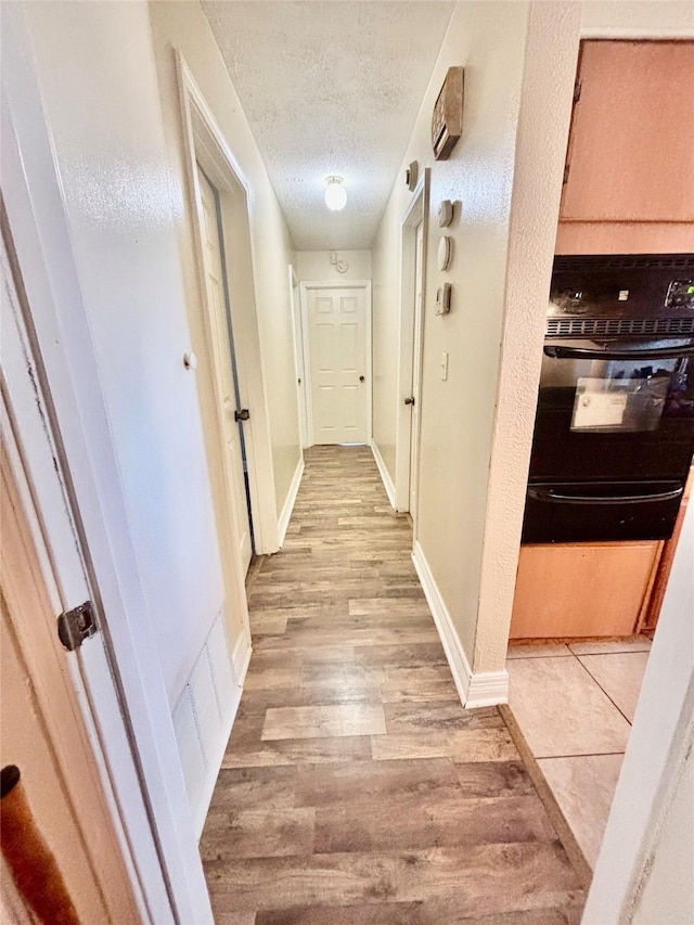 hallway with light wood-type flooring, baseboards, a textured ceiling, and visible vents