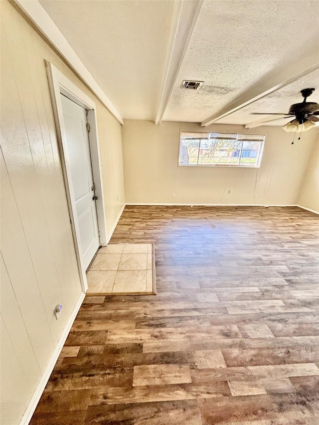 spare room featuring visible vents, beamed ceiling, a textured ceiling, wood finished floors, and ceiling fan