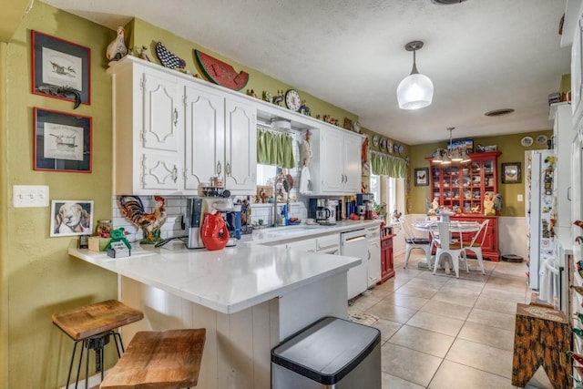 kitchen with a sink, white cabinetry, light tile patterned flooring, light countertops, and dishwasher