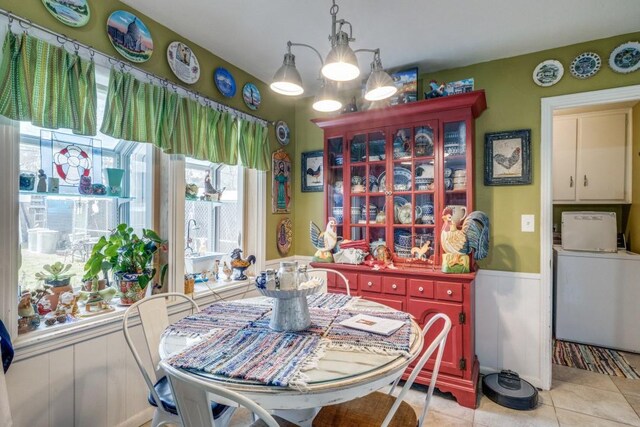 dining area featuring wainscoting, light tile patterned floors, washer / dryer, and an inviting chandelier