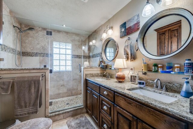 full bathroom with a textured ceiling, a shower stall, double vanity, and a sink