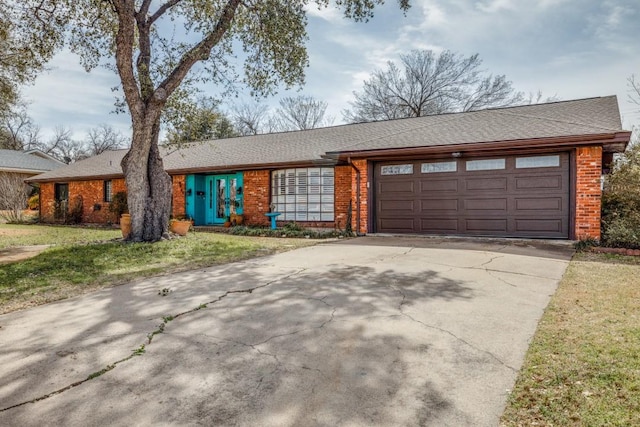 view of front of home featuring a front yard, a shingled roof, concrete driveway, a garage, and brick siding