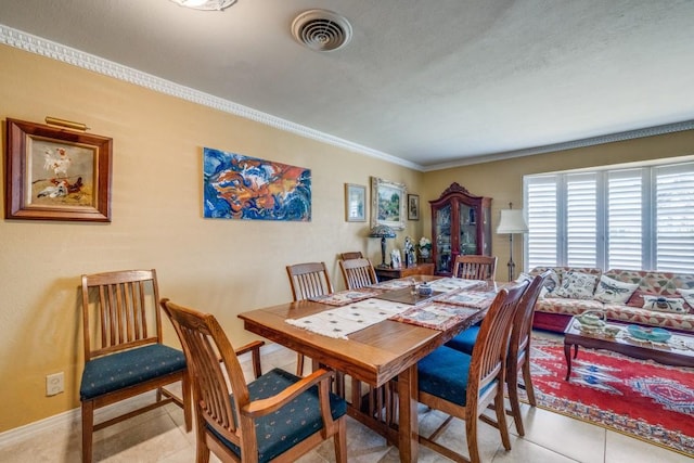 tiled dining space with visible vents, baseboards, and crown molding