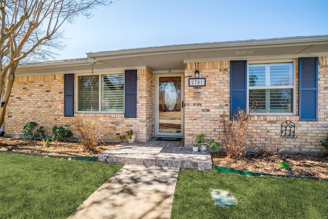 doorway to property featuring brick siding and a lawn