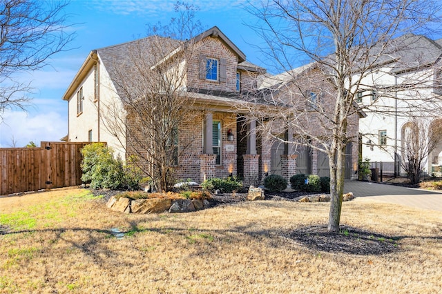 view of front of home featuring a front lawn, fence, brick siding, and driveway