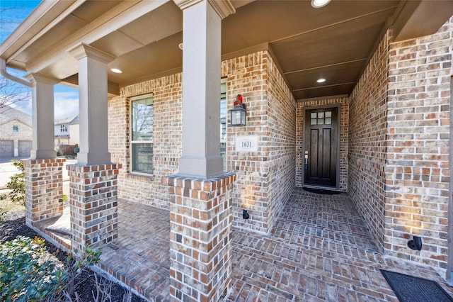 doorway to property featuring covered porch and brick siding