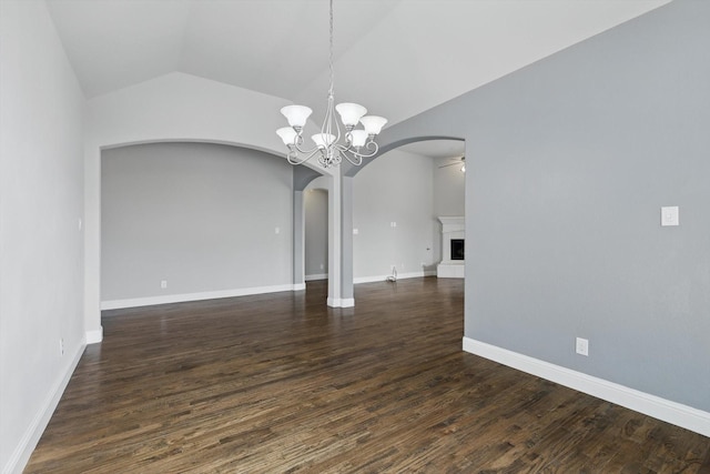 spare room featuring dark wood-type flooring, lofted ceiling, a fireplace with raised hearth, arched walkways, and baseboards