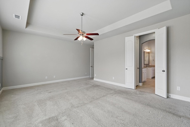 interior space featuring visible vents, light carpet, a raised ceiling, ensuite bathroom, and baseboards