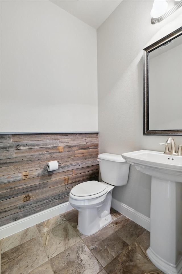 half bath with toilet, stone finish flooring, and baseboards