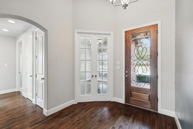 entrance foyer featuring arched walkways, french doors, dark wood-type flooring, and baseboards