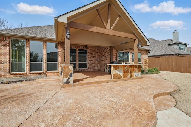 back of property with outdoor dry bar, a patio, fence, a shingled roof, and brick siding