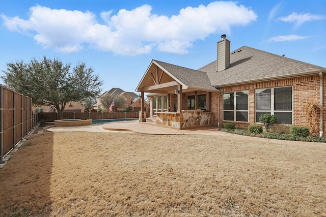 rear view of house with a patio area, brick siding, a fenced backyard, and roof with shingles